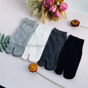May include: Four pairs of socks in different colors: gray, white, dark gray, and black. The socks are all ribbed and have a split toe design.