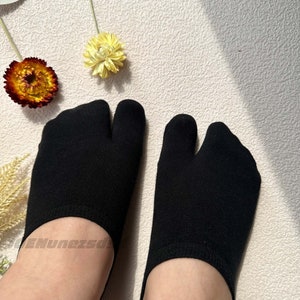 May include: A pair of black toe socks with a split toe design. The socks are made of a soft, breathable fabric and are ideal for wearing with sandals or flip-flops.
