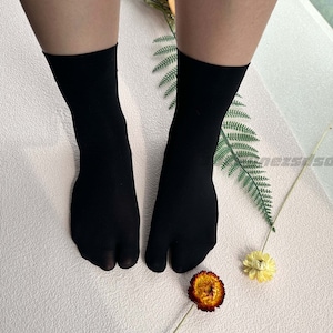 May include: A pair of black tabi socks with split toes. The socks are made of a soft, stretchy material and are perfect for wearing with sandals or other open-toe shoes.