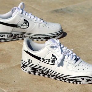 May include: White leather sneakers with black hand-drawn designs on the sides and soles. The designs include geometric shapes and lines.