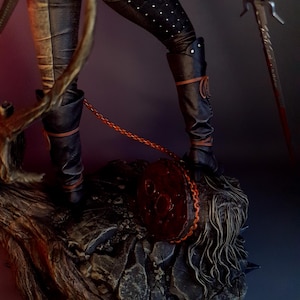May include: A detailed figurine of a character in black leather pants and boots, adorned with white dots. The figure holds a sword and stands on a textured, rocky base. A red circular object with a chain is also present.