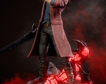May include: A detailed figurine of a character from the video game Devil May Cry, holding a gun and a sword. The figure is wearing a red coat and stands on a rocky base with glowing red elements. The figure has white hair and is in a dynamic pose.