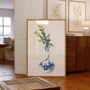 May include: A framed watercolor painting of a blue and white vase filled with a sprig of blueberries. The vase is decorated with a floral pattern. The painting is set against a white background.
