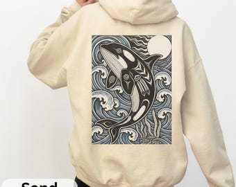 May include: Sand-colored hoodie featuring a black and white orca whale design on the back. The orca is depicted in a stylized illustration with ocean waves, a moon, and the word "Sand" at the bottom.