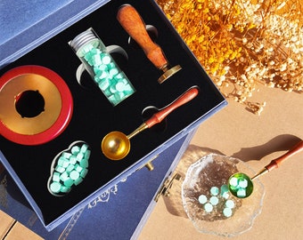 May include: A blue box with a variety of wax seal supplies, including a wooden handle, a metal spoon, a glass jar of wax beads, and a round wax seal stamp. The box is open and the supplies are visible.
