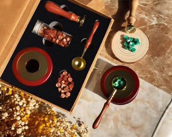 May include: A wooden box with a variety of wax seal supplies, including a wax melting pot, a spoon, wax beads, and a wax seal stamp. The box is open and the supplies are arranged neatly inside.