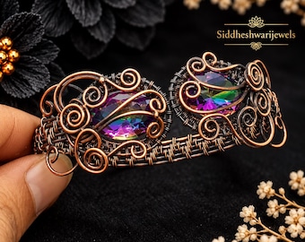 May include: A wire-wrapped cuff bracelet featuring two oval-shaped iridescent rainbow-colored gemstones set in dark copper-toned metal with intricate swirling wire patterns and the text Siddheshwarijewels visible in the upper right corner.