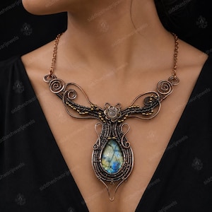 May include: A copper-toned wire-wrapped necklace featuring a central teardrop-shaped labradorite gemstone with blue and yellow iridescence. The metalwork includes intricate swirls, small metallic beads, and a floral accent at the top center.