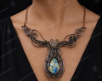 Può includere: Una collana in filo di rame avvolto con una pietra preziosa di labradorite a forma di goccia al centro, caratterizzata da iridescenze blu e gialle. La lavorazione del metallo include spirali complesse, piccole perline e un accento floreale.