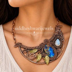 May include: A copper-toned wire-wrapped statement necklace featuring a large oval blue labradorite cabochon, a smaller pear-shaped moonstone, and three metallic gold-colored leaf charms. The text siddheshwarijewels is visible on the necklace.