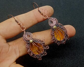 May include: A pair of copper wire earrings with amber glass stones. The earrings are teardrop shaped and have a delicate wire design.