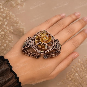May include: A copper-toned cuff bracelet featuring a central spiral ammonite fossil. The metal band is crafted with twisted wire detailing and decorative coiled accents on both sides. The fossil displays natural brown and tan tones.