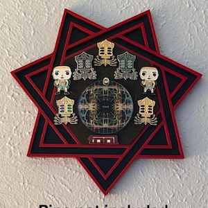 May include: A red and black seven-pointed star-shaped display stand with a circular center and six slots around the perimeter. The stand is designed to hold pins or other small collectibles. "Pins not included" is written below the stand.