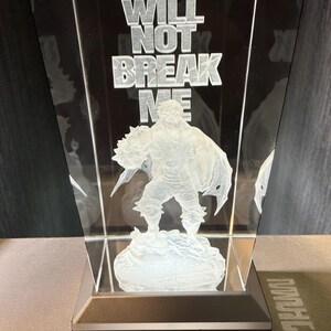 Puede incluir: Una escultura de vidrio transparente e iluminada con una figura y el texto "YOU WILL NOT BREAK ME". La escultura está montada sobre una base rectangular con un botón de encendido. La figura está grabada en el vidrio.