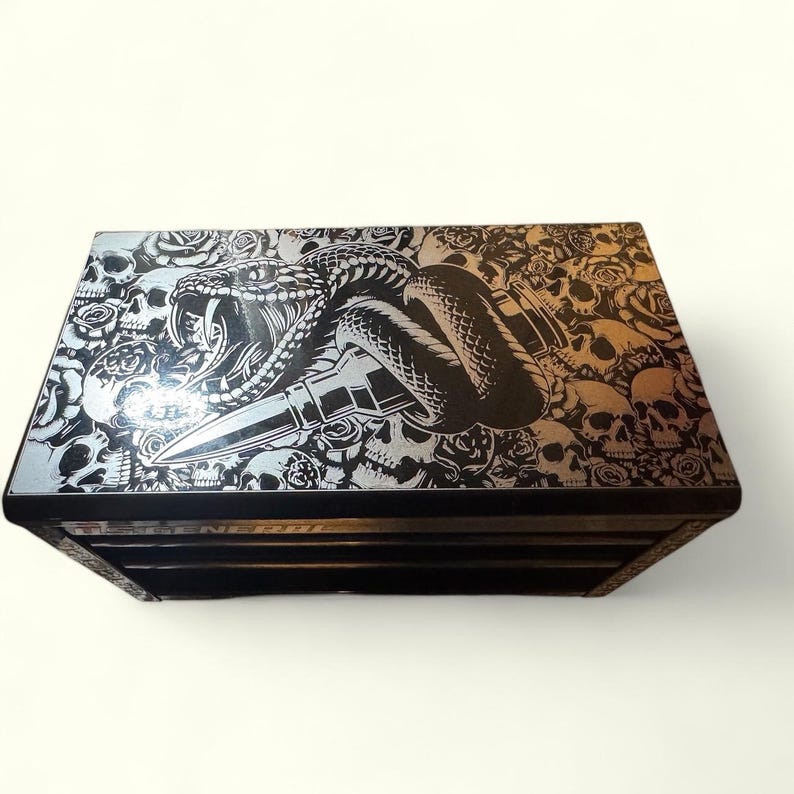 May include: Black metal toolbox with a silver skull, snake, and bullet design on the lid.