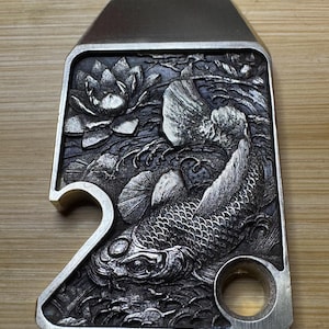May include: A silver metal bottle opener with a detailed design of a koi fish swimming through a lotus flower and water. The bottle opener has a hole for a key ring.