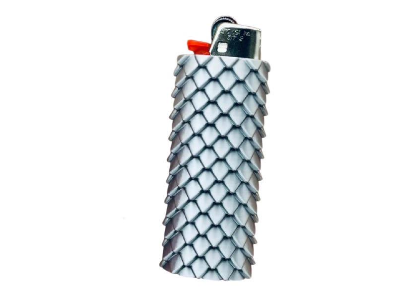 Puede incluir: Un encendedor plateado con una cubierta texturizada en forma de escamas. El encendedor tiene un bot&oacute;n de encendido rojo y una parte superior de metal. La cubierta est&aacute; hecha de peque&ntilde;as piezas superpuestas en forma de diamante, lo que le da una apariencia decorativa &uacute;nica.