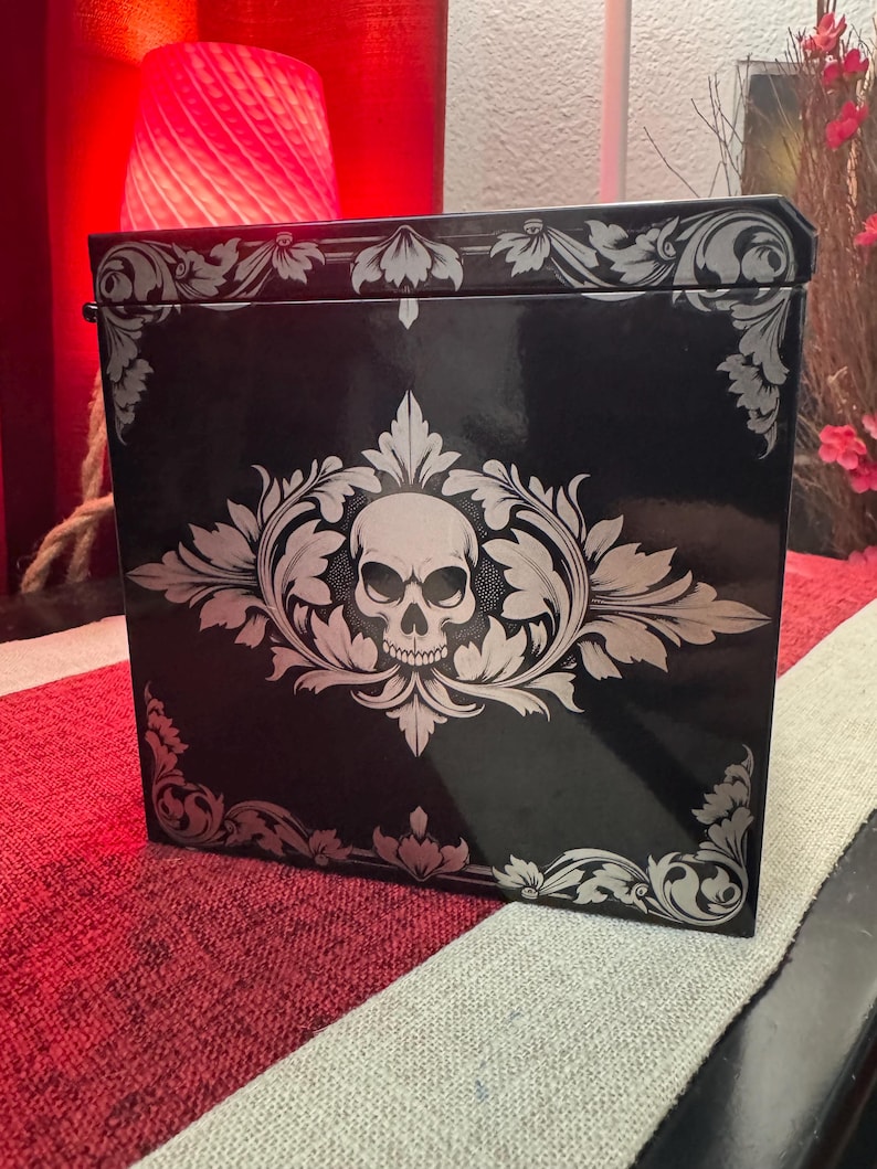 May include: Black box with a silver skull and floral design. The box has a glossy finish.