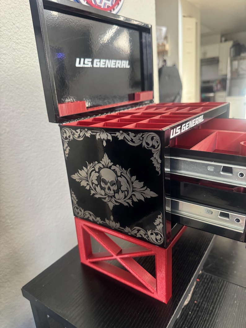 Puede incluir: Una caja de joyer&iacute;a negra y roja con un dise&ntilde;o de calavera y el texto "U.S. GENERAL" en la parte delantera. La caja tiene dos cajones y un compartimento superior con varios compartimentos.