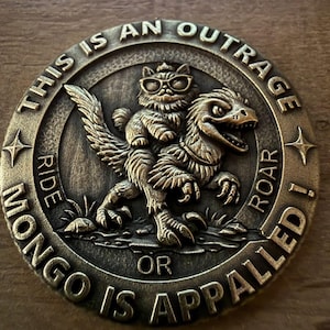 Puede incluir: Moneda de color bronce con un gato con gafas montado en un raptor. El borde de la moneda tiene el texto "THIS IS AN OUTRAGE RIDE OR MONGO IS APPALLED! ROAR!" Estrellas en el borde.
