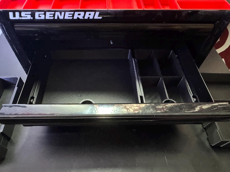 Puede incluir: Una caja de herramientas negra con un caj&oacute;n abierto, que revela un organizador compartimentado. La caja de herramientas tiene una tapa roja con las palabras "U.S. GENERAL" impresas en blanco.