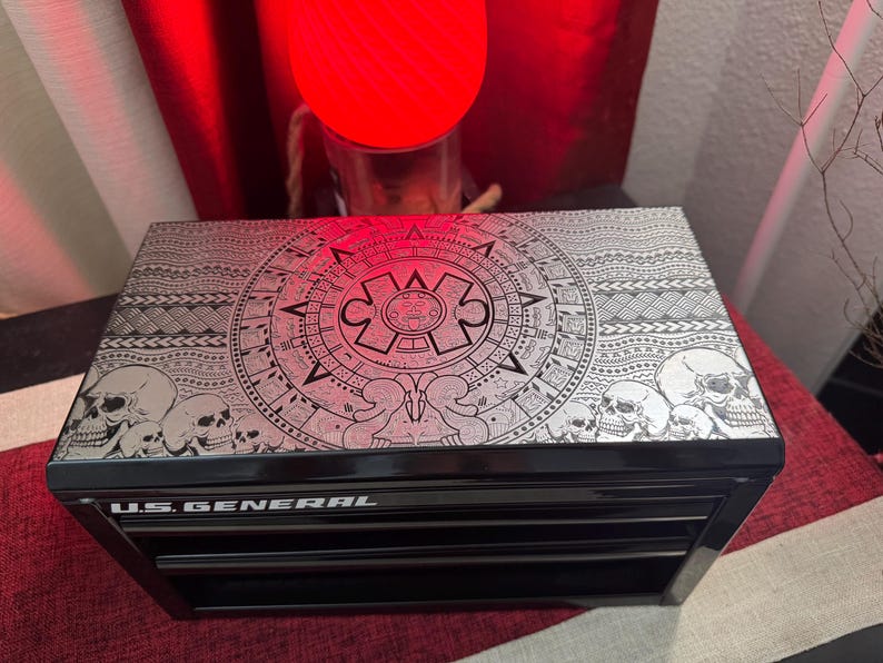May include: Black metal toolbox with three drawers. The top drawer has a decorative design featuring a circular pattern with skulls and a stylized Aztec calendar. The toolbox is labeled "U.S. GENERAL".