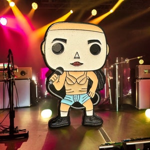 May include: A black and white pop culture figure of a person holding a microphone. The figure is wearing a light blue tank top and shorts. The figure is standing on a stage with a microphone stand and a speaker in the background.
