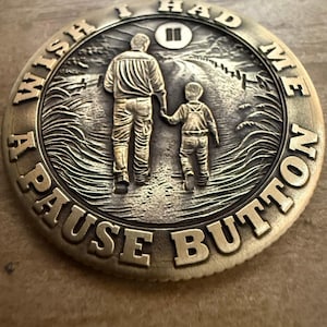 May include: A bronze-colored coin with the words "I WISH I HAD A PAUSE BUTTON" engraved around the edge. The coin features an embossed image of a person and a child walking together, holding hands. A pause symbol is above the figures.