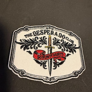May include: Embroidered patch with a white background and black border. The patch features the text "THE DESPERADO CLUB" and "SO FUN IT HURTS" with a dagger and scroll design. The patch is rectangular.