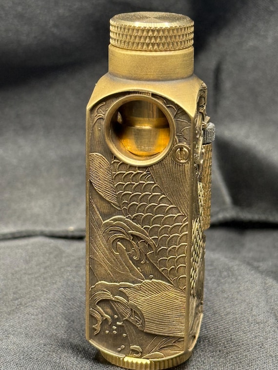 A hand-engraved brass torch lighter featuring intricate Koi & Lotus / Japanese wave motifs — functional EDC that doubles as a wearable piece of metalwork art.