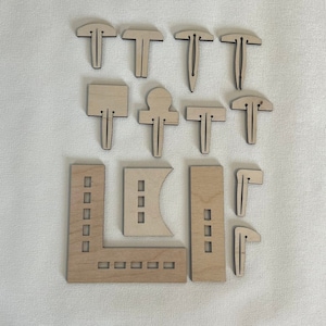 May include: A set of wooden craft shapes for creating a miniature house. The set includes various shapes, such as windows, doors, and roof pieces. The shapes are made of natural wood and have a light brown color.