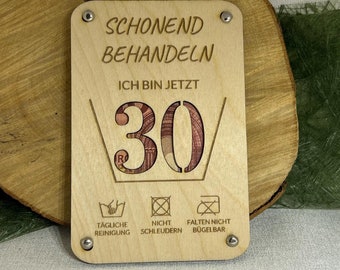 May include: A wooden sign with the text "Schonend Behandeln Ich Bin Jetzt 30" and care instructions: "Tägliche Reinigung", "Nicht Schleudern", "Falten Nicht Bügelbar".