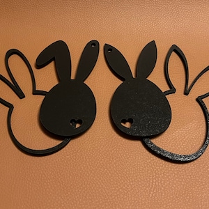 Könnte beinhalten: Zwei schwarze, bunnyförmige Wanddekorationen mit ausgeschnittenen Herzen. Die Bunnyformen sind schwarz umrandet und haben eine glatte, matte Oberfläche.