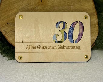 May include: A wooden card with a cutout of the number 30. The number is filled with a euro bill. The card has the text "Alles Gute zum Geburtstag" written on it.