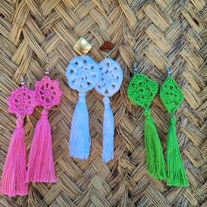 May include: Three pairs of crocheted earrings with tassels. The earrings are pink, white, and green. The tassels are long and flowing.