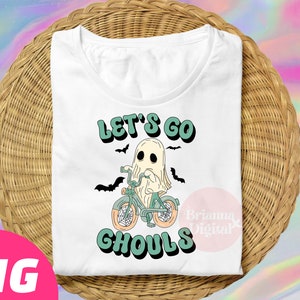 Könnte beinhalten: Weißes T-Shirt mit einer grünen und weißen Grafik eines Geistes, der ein Fahrrad fährt, mit dem Text "Let's Go Ghouls".