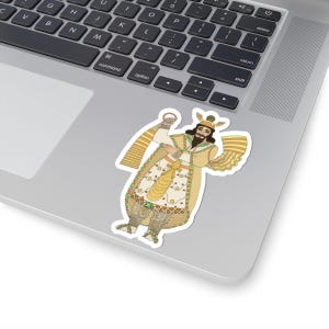 May include: A sticker featuring a detailed illustration of a figure in traditional attire. The design includes a long coat, a crown, and a beard, with a color palette of gold, cream, and brown. The sticker is placed on a laptop.