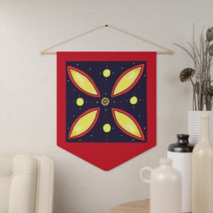 Könnte beinhalten: Ein roter Wandbehang mit geometrischem Design. Das Design zeigt vier gelbe blütenblattartige Formen auf einem dunkelblauen Hintergrund, mit gelben Kreisen und kleinen blauen Punkten. Der Behang wird an einer Holzstange aufgehängt.