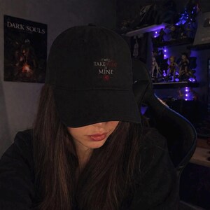 Könnte beinhalten: Eine schwarze Baseballkappe mit dem gestickten Text "I WILL TAKE WHAT IS MINE" in weißer und roter Schrift auf der Vorderseite. Die Kappe hat einen gebogenen Schirm und eine strukturierte Krone aus einem einfarbigen schwarzen Stoff.