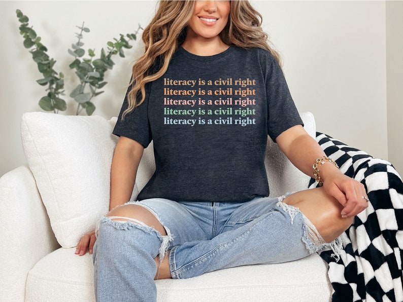 May include: A dark grey t-shirt with the text "literacy is a civil right" repeated five times in rainbow colours.