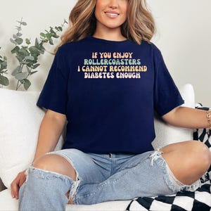 以下が含まれることがあります： レインボーカラーで「If you enjoy rollercoasters I cannot recommend diabetes enough」と書かれたネイビーブルーのTシャツです。