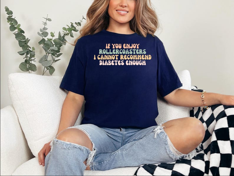 以下が含まれることがあります： レインボーカラーで「If you enjoy rollercoasters I cannot recommend diabetes enough」と書かれたネイビーブルーのTシャツです。