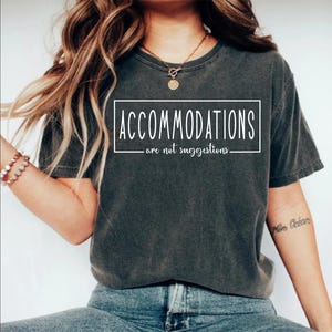 May include: A dark gray t-shirt with the text "ACCOMMODATIONS - are not suggestions -" printed in white.