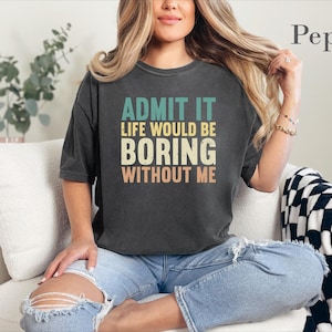 May include: A charcoal gray short-sleeve t-shirt featuring the text ADMIT IT LIFE WOULD BE BORING WITHOUT ME in stacked, multi-colored block lettering. The shirt has a crew neckline and a relaxed fit, with the word Pepper printed in the corner.