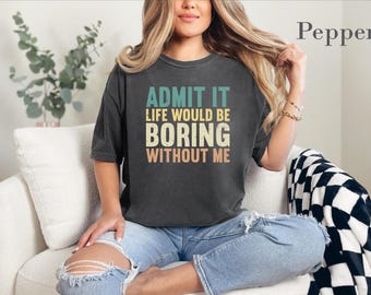 May include: A charcoal gray short-sleeve t-shirt featuring the text ADMIT IT LIFE WOULD BE BORING WITHOUT ME in stacked, multi-colored block lettering. The shirt has a crew neckline and a relaxed fit, with the word Pepper printed in the corner.