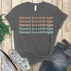May include: A heather grey t-shirt with the text "literacy is a civil right" repeated five times in different pastel colours.
