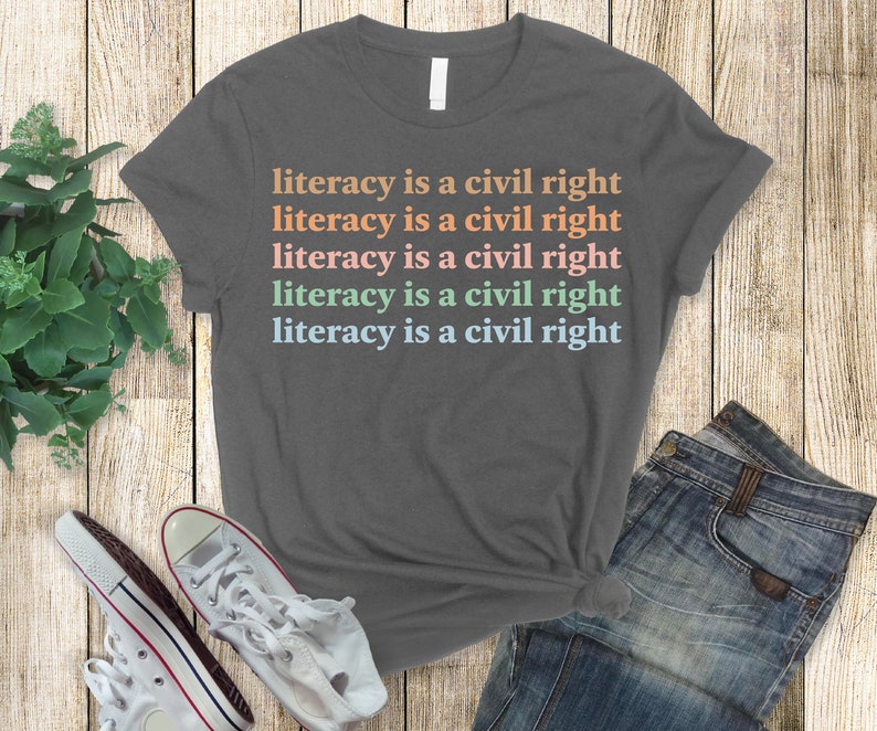 May include: A heather grey t-shirt with the text "literacy is a civil right" repeated five times in different pastel colours.