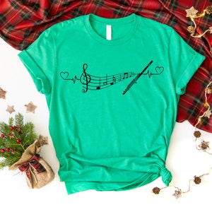 Może przedstawiać: Zielony T-shirt z czarnym nadrukiem przedstawiającym nutę muzyczną i flet z wzorem bicia serca. Nadruk głosi "Muzyka to moje bicie serca".
