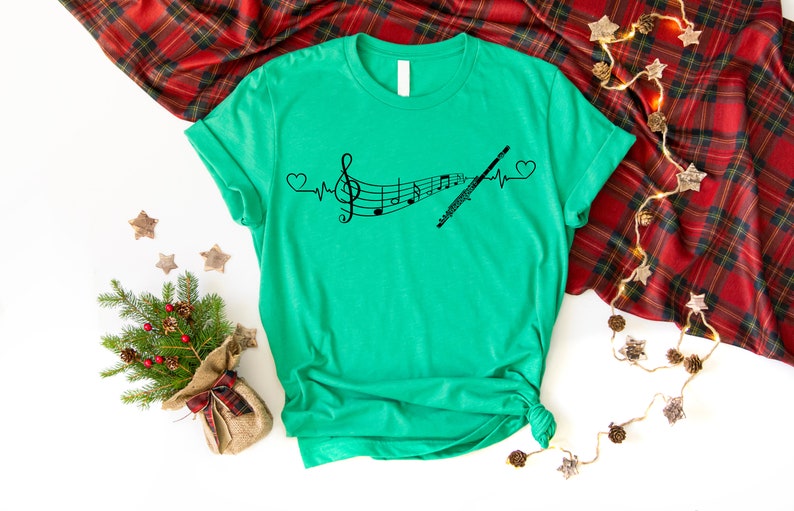 Może przedstawiać: Zielony T-shirt z czarnym nadrukiem przedstawiającym nutę muzyczną i flet z wzorem bicia serca. Nadruk głosi "Muzyka to moje bicie serca".