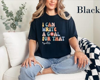 May include: A black short-sleeve t-shirt featuring the multi-colored text I CAN WRITE A GOAL FOR THAT with a small smiley face icon and the hashtag #spedlife printed in white script on the front chest area.